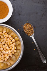 Boiled chickpeas in a bowl and spices on black metal background with place for text