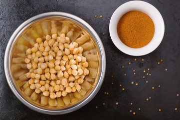 Boiled chickpeas in a bowl and spices on black metal background