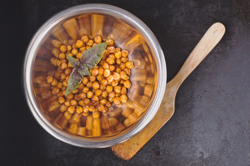 Chickpeas baked with spices in metal bowl and wooden spatula on black surface with place for text
