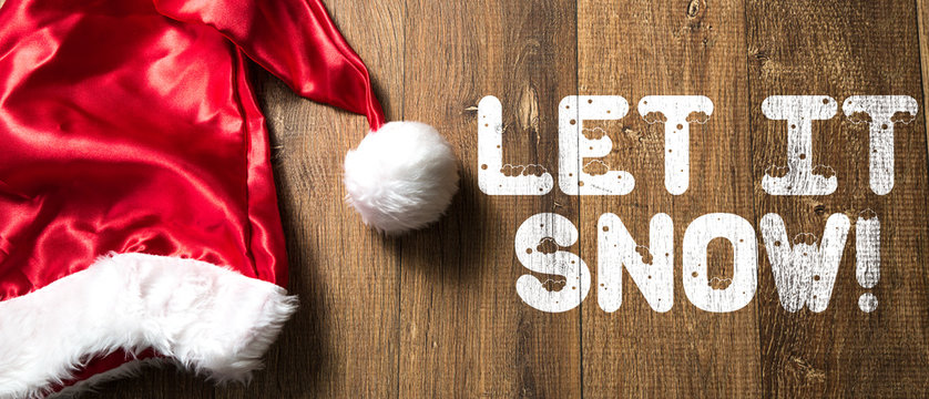 Let It Snow written on wooden background with Santa Hat