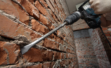 Man's hands holding plugger against the brick wall