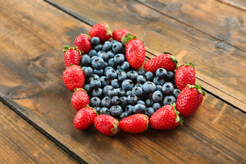 Heart shaped strawberries and blueberries on wooden background