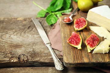 Ripe figs and cheese on cutting board, on wooden background