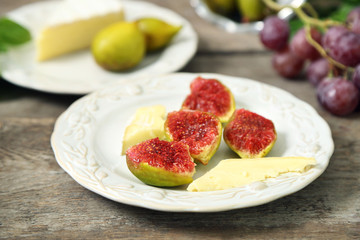 Ripe figs and cheese on plate, on wooden background