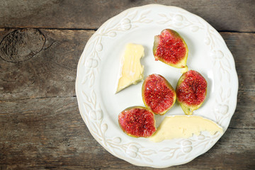 Ripe figs and cheese on plate, on wooden background