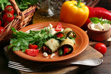 Zucchini rolls with cheese, bell peppers and arugula on plate, close-up, on table background