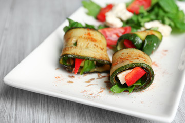 Zucchini rolls with cheese, bell peppers and arugula on plate, close-up, on table background