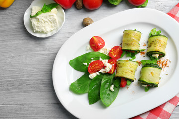 Zucchini rolls with cheese, bell peppers and arugula on plate, close-up, on table background