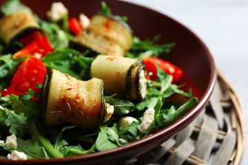 Salad with arugula and zucchini rolls on plate, on table background
