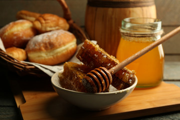 Honeycombs on plate, hot buns in basket on wooden background