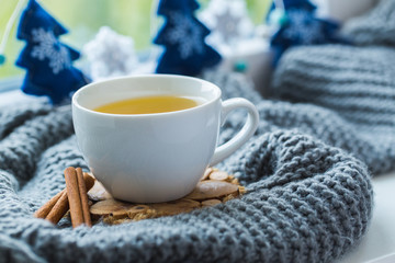 Obraz na płótnie Canvas White cup of chamomile tea with grey scarf on the windowsill.