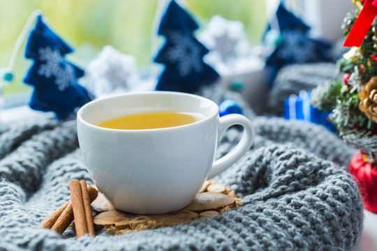 White cup of chamomile tea with grey scarf on the windowsill.