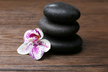 Obraz na płótnie Canvas Black pebbles with orchid on wooden background