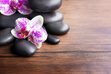 Obraz na płótnie Canvas Black pebbles with orchid on wooden background