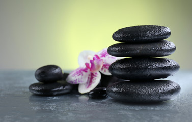 Naklejka na ściany i meble Black pebbles with orchid on grey table, close up