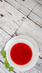 A cup of hibiscus tea and fresh mint leaves over wooden background