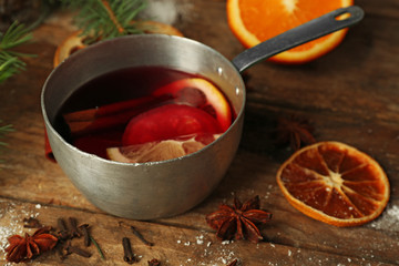 Mulled wine in stew-pan on decorated wooden background