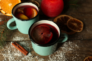 Decorated composition of mulled wine in mugs on wooden table