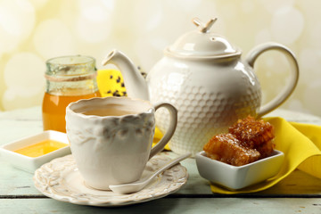 Honeycomb, bowl with honey, teapot on color wooden background