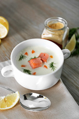 Delicious salmon cream soup on wooden table, which served with sliced lemon and spices