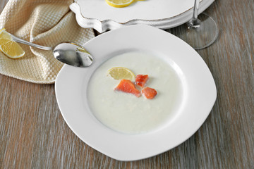 Served wooden table with tasty salmon cream soup, wine and lemon on it, close up
