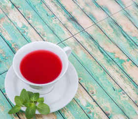 Fototapeta na wymiar A cup of hibiscus tea and fresh mint leaves over wooden background