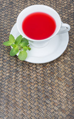 A cup of hibiscus tea and fresh mint leaves over wicker background