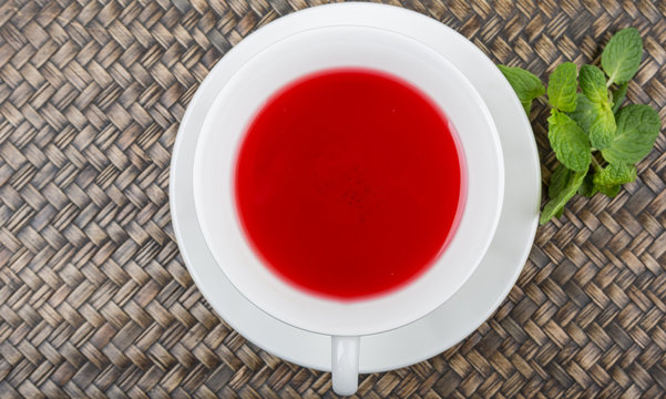 A cup of hibiscus tea and fresh mint leaves over wicker background