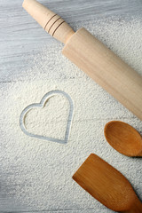 Heart of flour and kitchen utensils on wooden background