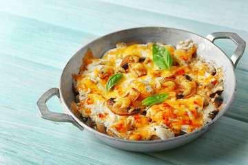 Roasted mushrooms, chicken and cheese gratin in pan, on wooden background