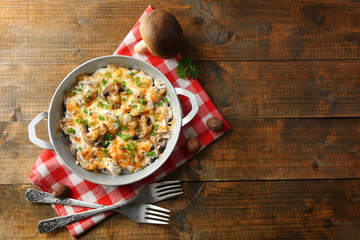 Roasted mushrooms, chicken and cheese gratin in pan, on wooden background