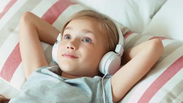 Closeup portrait girl child listening music in headphones with eyes closed and lying on the bed