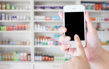 hand using smartphone with blur shelves of drugs in the pharmacy
