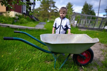 Cute young baby boy near wheelbarrow in garden