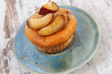 Fresh baked muffins with plums on plate on old wooden background, delicious dessert