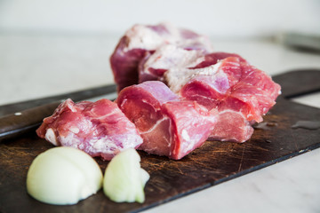 the cut meat, onions and steel knife on a wooden chopping board