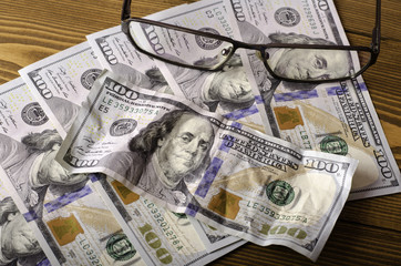 Glasses on top of the $ 100 bills and crumpled $ 100 bill .