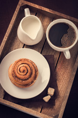cinnamon roll,  cup of coffee and cream  on wooden tray