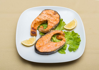 Dish of grilled red fish salmon steak with lettuce and lemon (focus is in the middle of the dish)