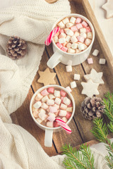 Mugs with hot chocolate, murshmallow and candy cane on wooden tr