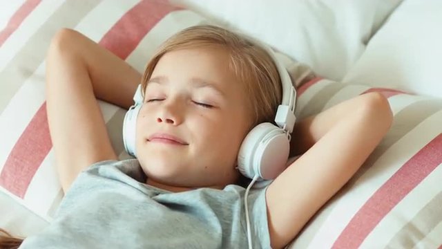 Closeup portrait girl listening music in headphones with eyes closed and lying on the bed