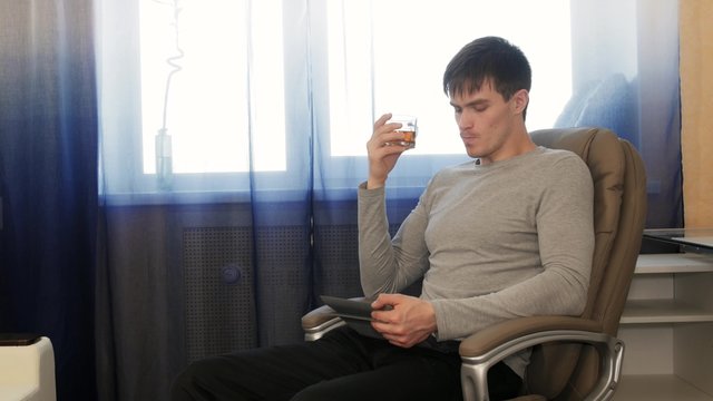 Man with tablet pc sitting on chair, drinking tea