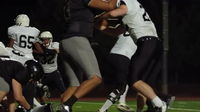 A football player gets tackled on his way to the end zone at night