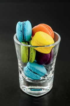 Sweet and colourful french macaroons in glass cup on a black background.