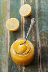 Lemon curd in glass jar on rustic wooden table, traditional fruit cream, vintage style, top view