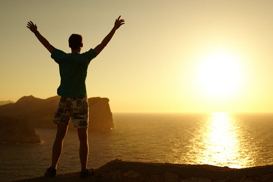 Silhouette of a young man with hands raised in the sunset. Cocept on winner. Success. Explorer. Man at Cap Formentor, Majorca