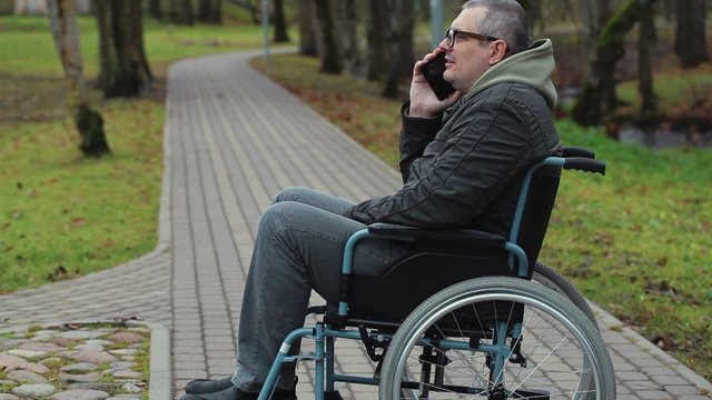 Disabled man in wheelchair on path talking on smartphone