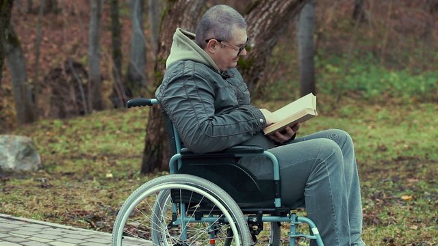 Disabled man reading book in wheelchair at outdoor
