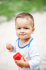 Cute brown-eyed little boy playing with a red plastic toy car