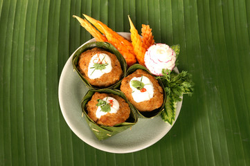 red curry mixed spicy herb with meat in banana leaf decoration by carving carrot and radish on banana leaf background 
